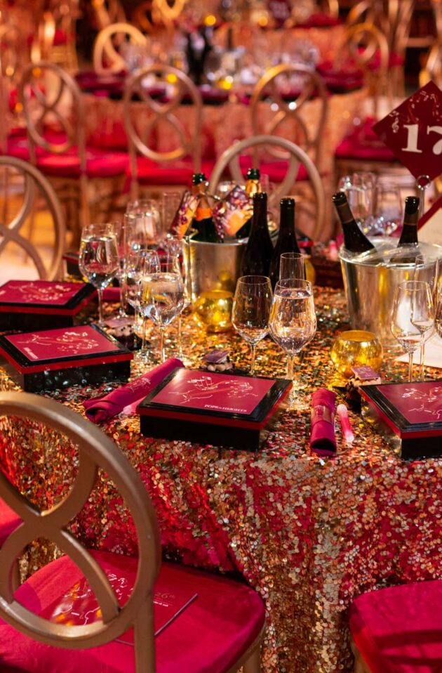 Elegant banquet table setting with red and gold theme, crystal glassware, and numbered table marker, curated by expert event planners.