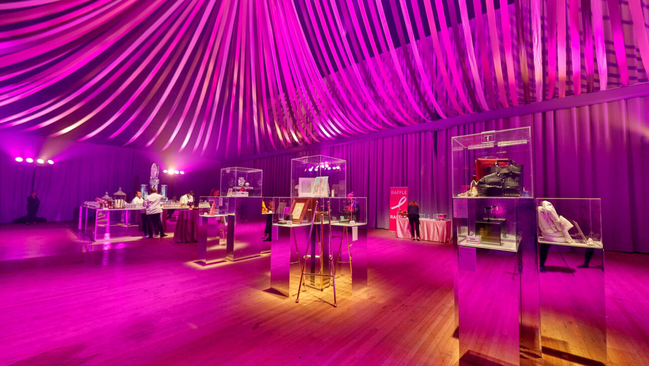 Elegant event venue space with a purple lighting scheme, draped ceiling decorations, and display tables with exhibits.