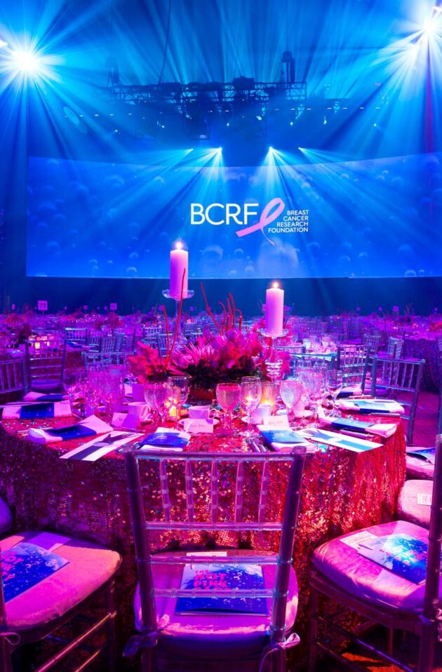 Elegant gala dinner setting with blue lighting and BCRF event branding onstage hosted by a leading event planning company.