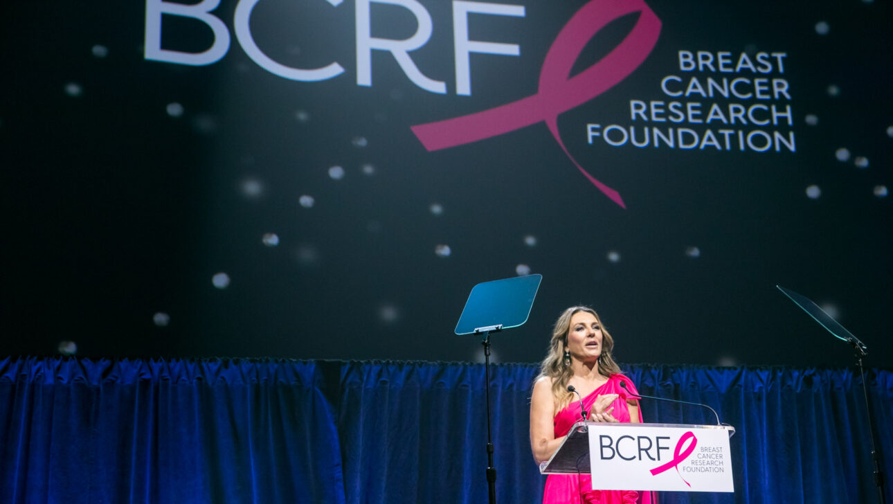 A woman speaks at a podium bearing the breast cancer research foundation logo at a charitable event organized by an event planning company.