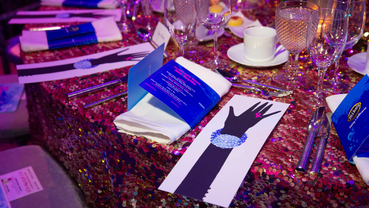 A decorated event table arranged by an event planning company with a sequined tablecloth, place settings, and event programs.
