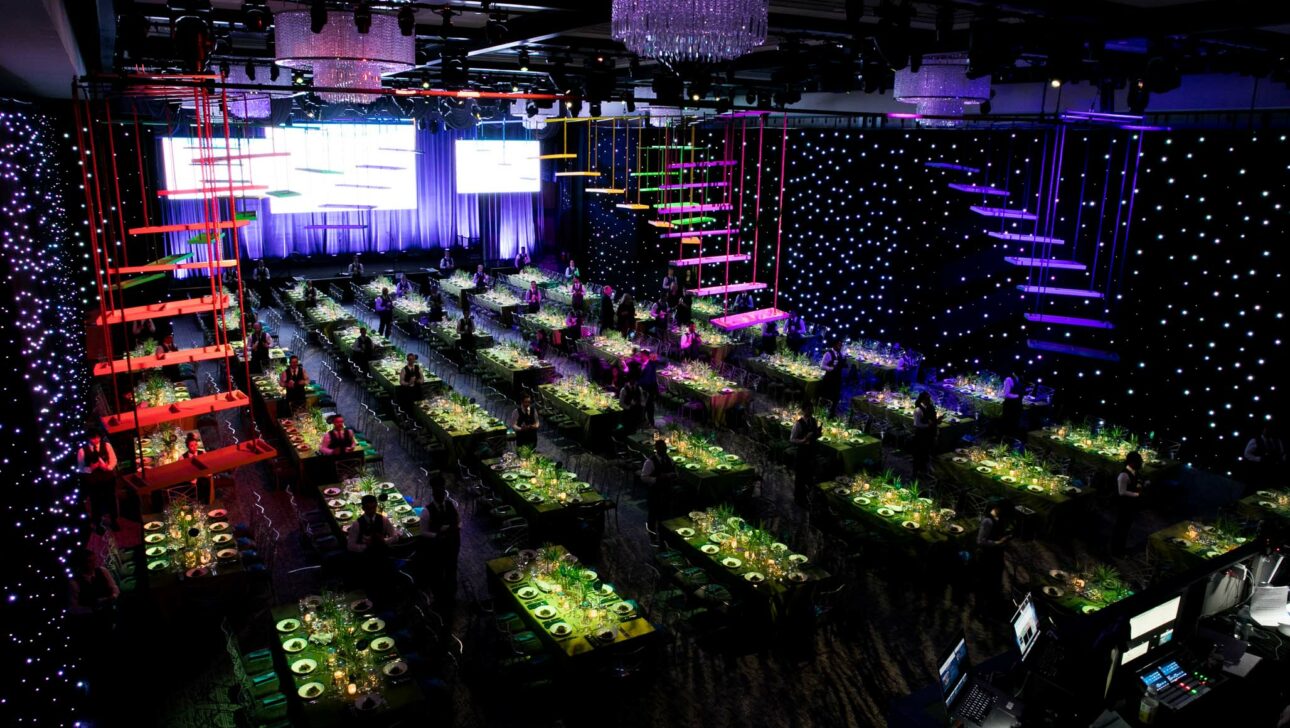 Elegant event venue space set up for a formal dinner with colorful lighting and a stage with large screens.