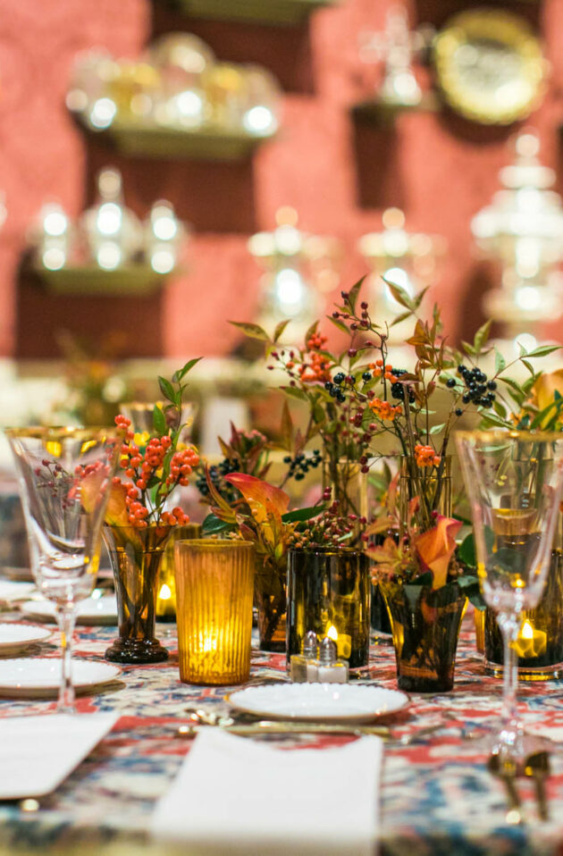 Elegant dining table set with floral centerpieces, fine glassware, and ornate silver in a richly decorated event venue space.