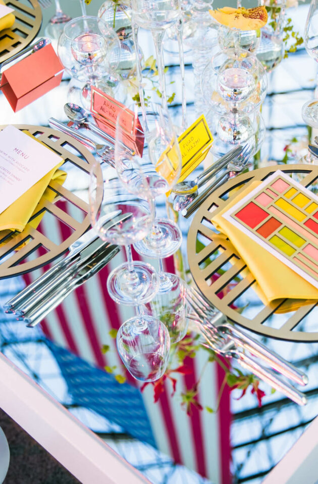 Elegant table setting with geometric placemats, fine glassware, and folded menus at a formal event venue space.