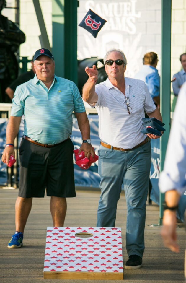 Two men playing a game of cornhole at an outdoor event organized by an event planning company.