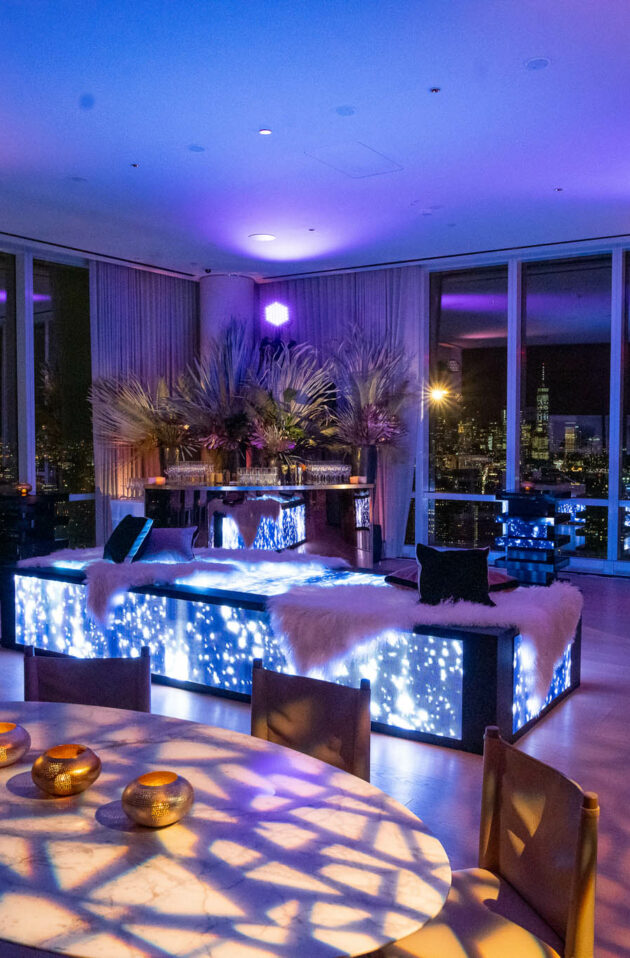 Chic event venue space with ambient lighting and cityscape views through floor-to-ceiling windows.