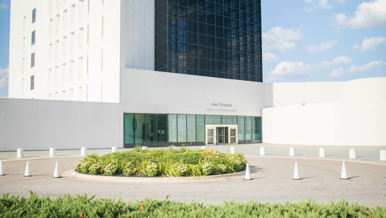 Modern event venue space with a large glass facade and white walls under a clear blue sky.