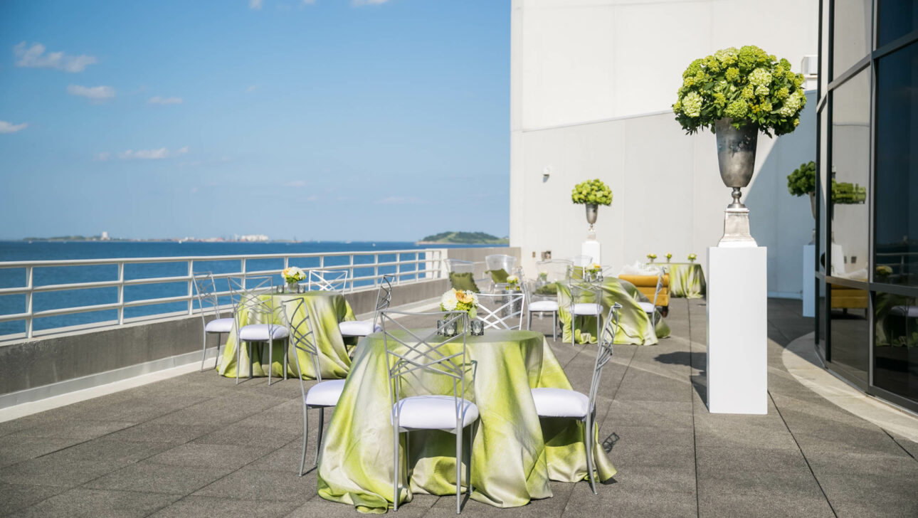 Outdoor event venue space setup with decorated tables and a sea view.