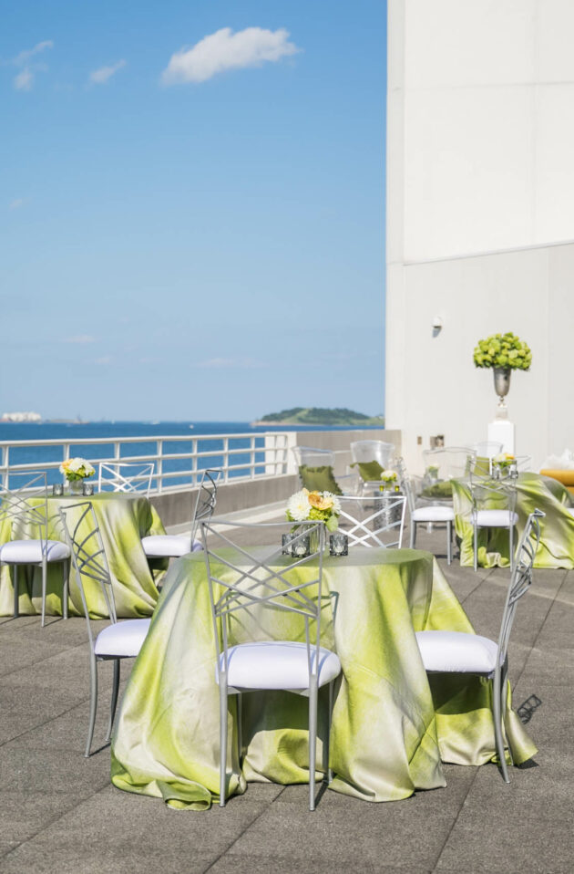 Outdoor event venue space setup with decorated tables and a sea view.