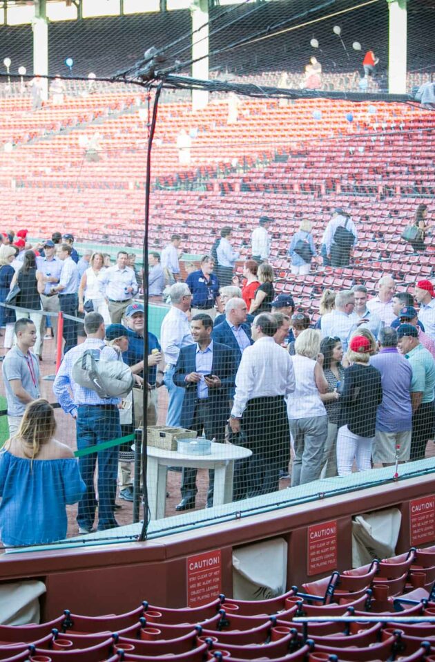 Group of people mingling in a baseball stadium, an event venue space, with empty red seats in the foreground.