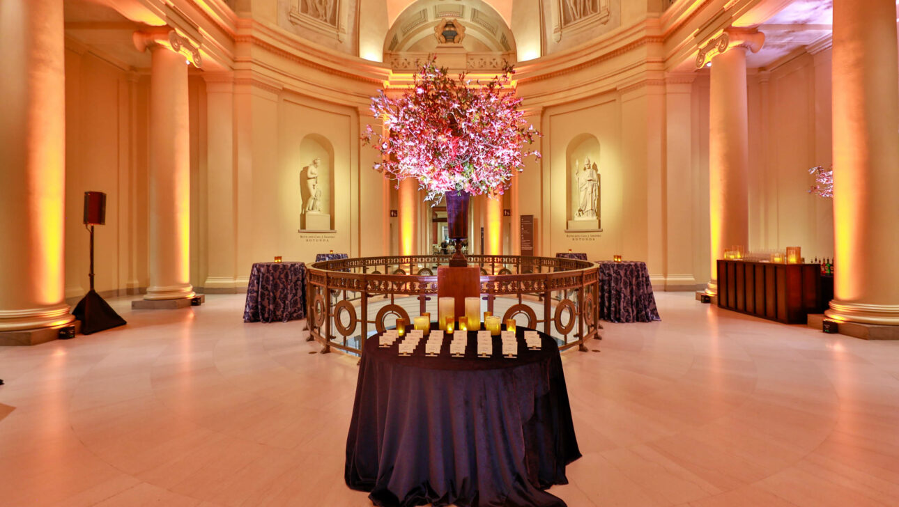 Elegant event venue space with a large floral centerpiece, ambient lighting, and tables draped with tablecloths.