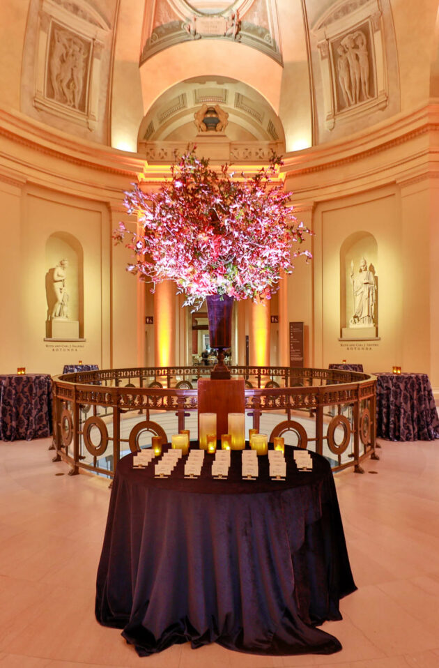 Elegant event venue space with a large floral centerpiece, ambient lighting, and tables draped with tablecloths.