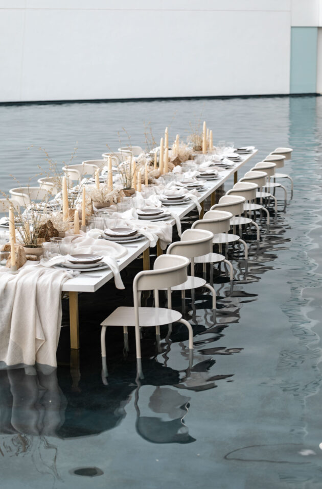 Elegantly set dining table, orchestrated by skilled event planners, partially submerged in water with chairs and decorative grass centerpieces.