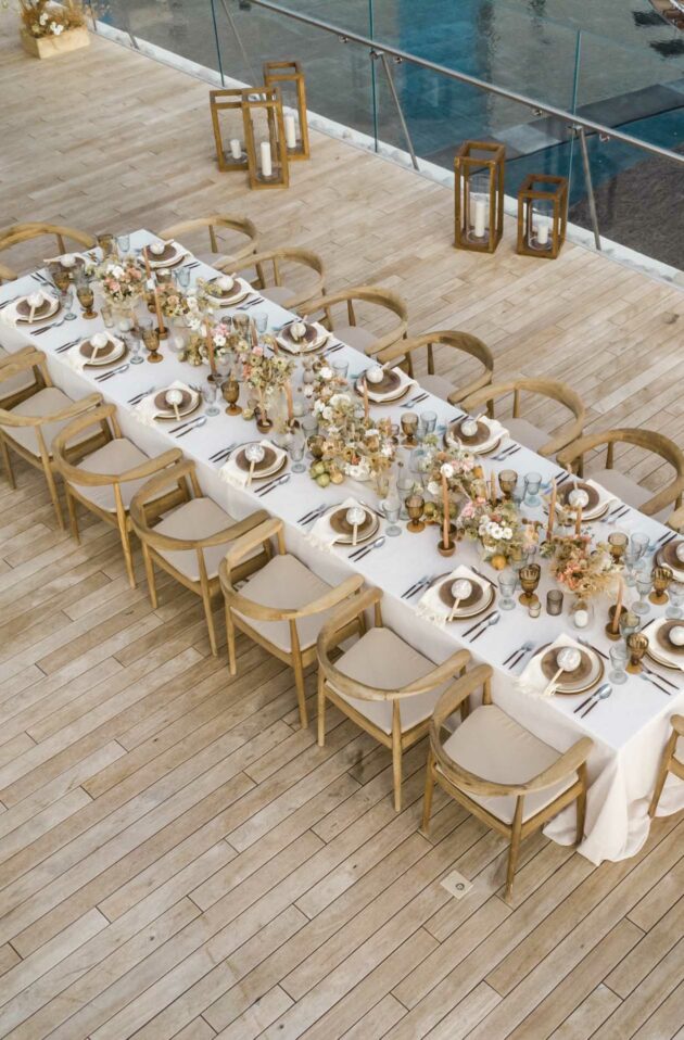 An elegantly set outdoor dining table prepared by a top event planning company, with decorative centerpieces and place settings, overlooking a pool area.