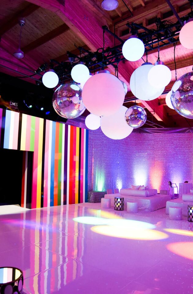 Event venue space vibrantly lit with colorful stripes, hanging orbs, and disco balls.