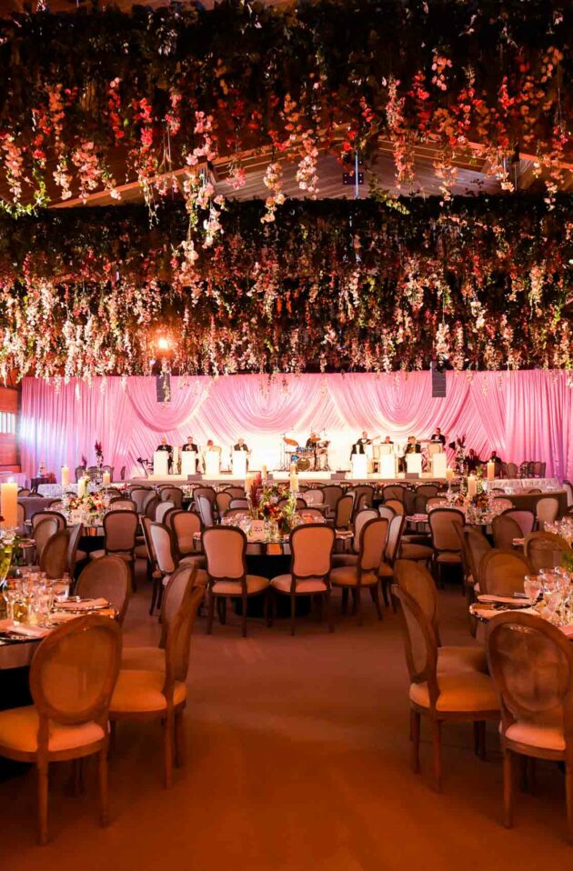 Elegant banquet hall adorned with floral arrangements and a pink draped backdrop, set up by an event planning company for a formal event.