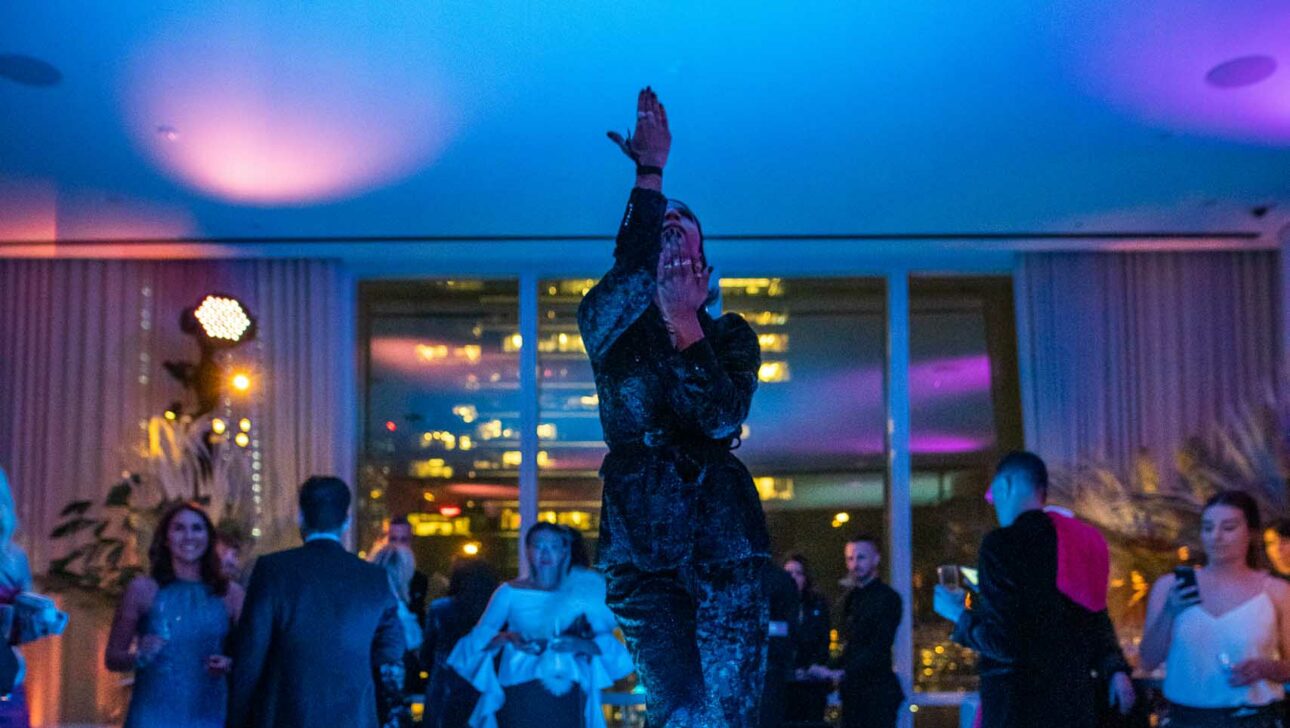 Performer dancing on a lit-up stage at an evening event organized by an event planning company with onlookers in the background.