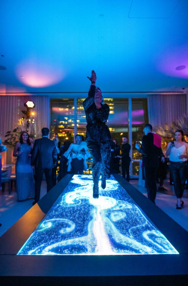 Performer dancing on a lit-up stage at an evening event organized by an event planning company with onlookers in the background.