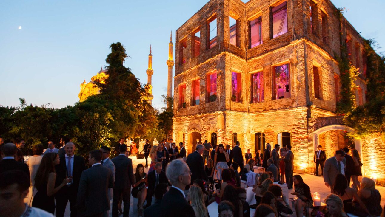 Guests gathered for an evening event outside a historic building illuminated by warm lighting with a minaret visible in the background, meticulously organized by an event planning company.
