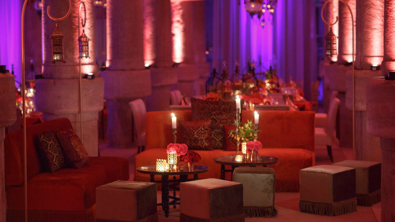 Elegant event venue space with warm lighting, decorated with Moroccan-style cushions, lanterns, and floral centerpieces.