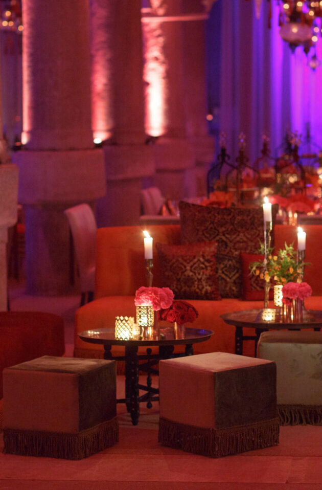 Elegant event venue space with warm lighting, decorated with Moroccan-style cushions, lanterns, and floral centerpieces.