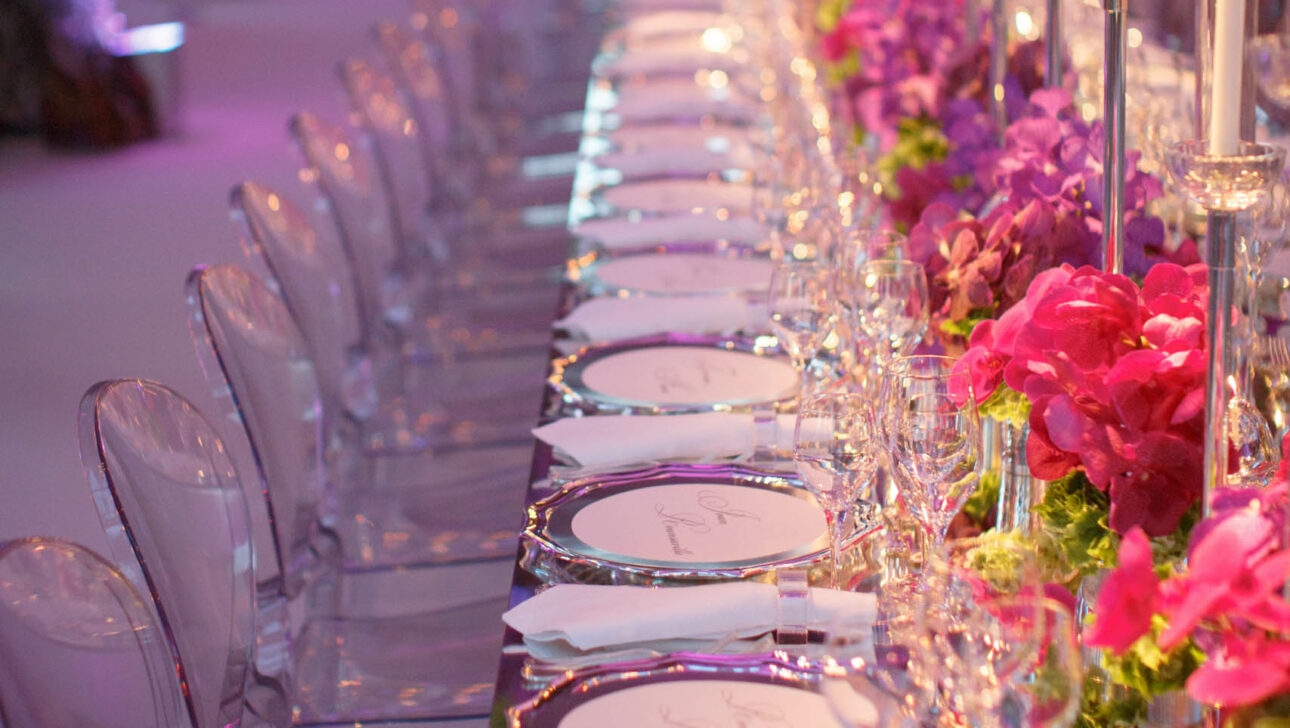 An elegantly set banquet table with tall candles and pink floral arrangements, meticulously arranged by a premier event planning company.