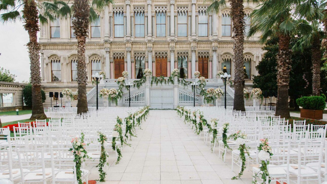 Elegant outdoor wedding setup managed by an event planning company, with white chairs and floral decorations in front of a classic architectural building.