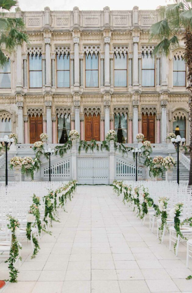 Elegant outdoor wedding setup managed by an event planning company, with white chairs and floral decorations in front of a classic architectural building.